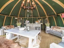 An interior of a wooden hut with a table, two sofas, a bar counter, decorative plants, and a ceiling chandelier at Lillie's Shepherds Hut at Shepherds Lodge in Bottesford near Redmile and Vale of Belvoir