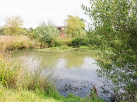 A small pond with water plants and surrounded by grass and trees with a wooden structure in the background at Lillies Shepherds Hut at Shepherds Lodge in Bottesford near Redmile and Vale of Belvoir