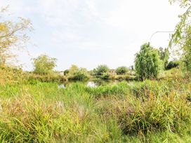 A pond surrounded by grass and trees with a bridge in the background at Lillie's Shepherds Hut at Shepherds Lodge Bottesford near Redmile and Vale of Belvoir