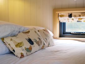 A bed with patterned pillows and a window with curtains at Lillie's Shepherds Hut at Shepherds Lodge Retreat and Wellness in Bottesford near Redmile and Vale of Belvoir