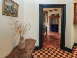 A hallway with a wooden table and vase with dried plants overlooking a room with terracotta floor and blue stove at The Gables in Spaxton near Nether Stowey