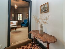 A small table with a vase and dried plants near a doorway leading to a room with a blue armchair and a white sofa at The Gables in Spaxton near Nether Stowey