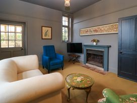 A living room with a cream sofa blue armchair floral small table fireplace and a television at The Gables in Spaxton near Nether Stowey