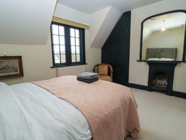 A bedroom with a bed covered with a pink quilt and folded towels a window a chair a fireplace with a mirror above and a framed picture on the wall at The Gables in Spaxton near Nether Stowey