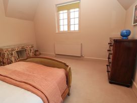 A bedroom with a bed covered with a blanket a wooden chest of drawers with a blue vase and a dressing table with floral skirt at The Gables in Spaxton near Nether Stowey