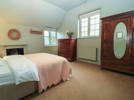 A bedroom with a bed a wooden dresser a wardrobe with mirror and two windows at The Gables in Spaxton near Nether Stowey