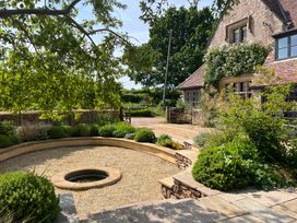 A garden with a circular gravel area and water feature next to a stone house with greenery at The Gables in Spaxton near Nether Stowey