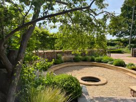 A garden with gravel ground and a circular stone water feature surrounded by greenery and a tree at The Gables in Spaxton near Nether Stowey
