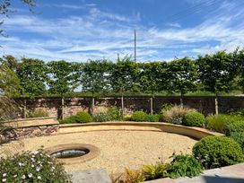 A garden with a circular gravel area surrounded by plants trees and a low curved stone wall at The Gables in Spaxton near Nether Stowey