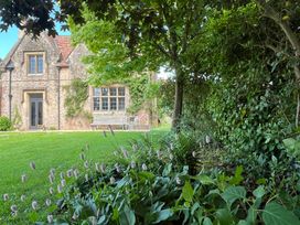 A garden with flowers and trees in front of a stone house at The Gables in Spaxton near Nether Stowey