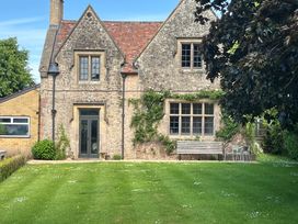 An exterior view of a stone house with a lawn a bench and chairs at The Gables in Spaxton near Nether Stowey