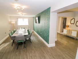 A dining room with a table and chairs next to a green patterned wall with a mounted TV at Bwthyn Y Mor in Tal-Y-Bont