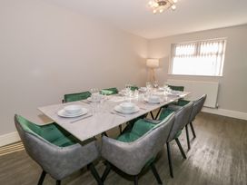 A dining room with a rectangular table set for eight and green and gray chairs at Bwthyn Y Mor in Tal-Y-Bont