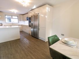 A kitchen with white cabinets a stainless steel refrigerator a white island and a dining table with a green chair at Bwthyn Y Mor in Tal Y Bont