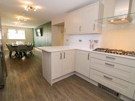 A kitchen with white cabinets and gas stove connected to a dining area with a table and chairs at Bwthyn Y Mor in Tal-Y-Bont