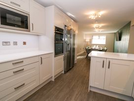 A kitchen with white cabinets stainless steel appliances and a dining area with a table and chairs at Bwthyn Y Mor in Tal-Y-Bont