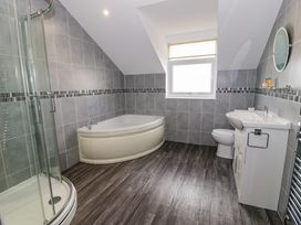 A bathroom with a corner bathtub a shower enclosure a toilet a sink with a cabinet and a window at Bwthyn Y Mor in Tal Y Bont