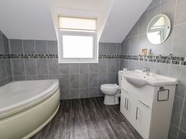 A bathroom with a corner bathtub toilet sink with cabinet and a window at Bwthyn Y Mor in Tal Y Bont