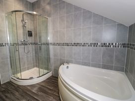 A bathroom with a corner shower enclosure and a corner bathtub with tiled walls and wood effect flooring at Bwthyn Y Mor in Tal-Y-Bont