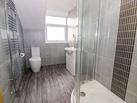 A bathroom with a toilet sink shower enclosure with glass doors tiled walls and wood effect flooring at Bwthyn Y Mor Tal Y Bont