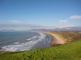 A coastal landscape with a sandy beach and waves next to grassy dunes and hills at Bwthyn Y Mor in Tal-Y-Bont