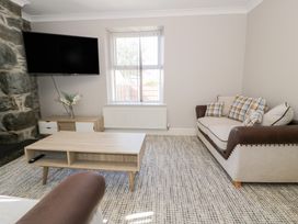 A living room with a plaid cushion sofa a coffee table a wall-mounted TV and a sideboard with flowers at Bwthyn Y Mor in Tal-Y-Bont