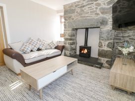 A living room with a sofa with checked cushions a wooden coffee table a stone fireplace with a wood-burning stove and a wooden side table with flowers at Bwthyn Y Mor in Tal-Y-Bont