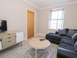 A living room with a black sofa a round wooden coffee table and a wooden cabinet with a television at Bwthyn Y Mor in Tal Y Bont
