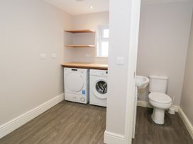 A laundry room with a washing machine dryer and shelves next to a small bathroom with a toilet and sink at Bwthyn Y Mor in Tal Y Bont