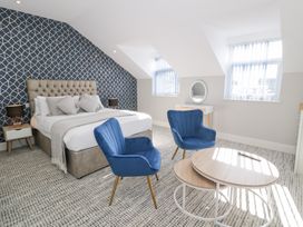 A bedroom with a bed two blue chairs a round wooden table and windows at Bwthyn Y Mor in Tal-Y-Bont