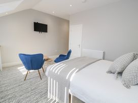 A bedroom with a bed pillows blue chairs a round wooden table and a wall-mounted television at Bwthyn Y Mor in Tal-Y-Bont