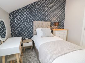 A bedroom with a single bed a bedside table with a lamp a chest of drawers a vanity table and a patterned wall at Bwthyn Y Mor in Tal-Y-Bont
