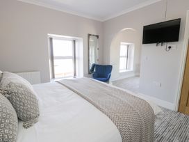 A bedroom with a bed with pillows and a blanket a blue chair a wall mirror a wall-mounted television and two windows at Bwthyn Y Mor in Tal-Y-Bont