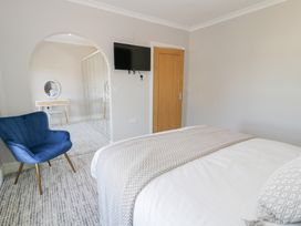 A bedroom with a bed a blue chair a wall mounted TV and an archway leading to a dressing area at Bwthyn Y Mor in Tal-Y-Bont