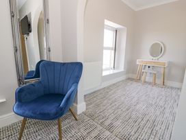 A room with a blue upholstered chair a large framed mirror a window and a dressing table with a round mirror at Bwthyn Y Mor Tal-Y-Bont