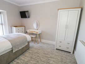 A bedroom with a bed a chest of drawers a wall mounted tv a dressing table with a mirror a stool and a wardrobe at Bwthyn Y Mor in Tal-Y-Bont