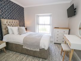 A bedroom with a bed next to a window a chest of drawers a small desk with a stool and a wall-mounted tv at Bwthyn Y Mor in Tal-Y-Bont