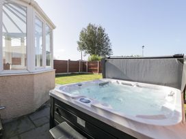 An outdoor hot tub next to a conservatory and garden with a tree and wooden fence at Bwthyn Y Mor in Tal-Y-Bont