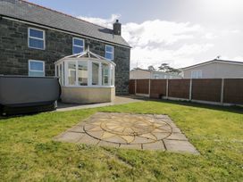 A garden with a stone patio and a stone house with a conservatory at Bwthyn Y Mor in Tal-Y-Bont