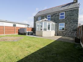 A stone house with a white conservatory and a grassy backyard with a hot tub at Bwthyn Y Mor in Tal-Y-Bont