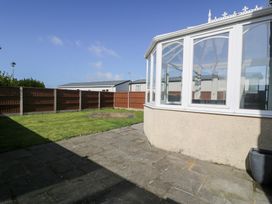 A paved patio area next to a glass conservatory and a grass lawn surrounded by a wooden fence at Bwthyn Y Mor in Tal-Y-Bont
