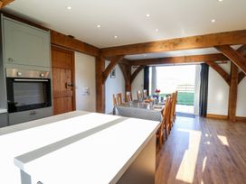 A dining area with a long table set with cups and plates wooden chairs exposed wooden beams and a kitchen oven at Yr Adfa in Llangeitho near Tregaron