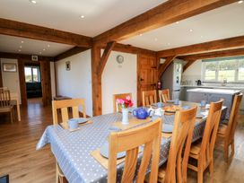 A dining area with a table covered in a polka dot tablecloth and wooden chairs in a room with wooden beams and a kitchen in the background at Yr Adfa in Llangeitho near Tregaron