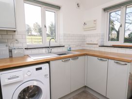 A kitchen corner with a washing machine under a wooden countertop and a double sink under two windows at Yr Adfa in Llangeitho near Tregaron