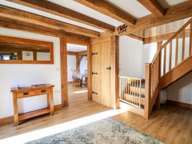 An interior hallway with wooden beams wooden floor a small wooden table with papers a wooden staircase with a baby gate and a doorway to a dining area at Yr Adfa Llangeitho near Tregaron