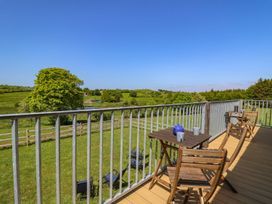 A balcony with wooden chairs and tables overlooking green fields and trees at Yr Adfa in Llangeitho near Tregaron