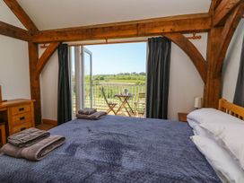A bedroom with a bed covered in blue blanket and folded towels on top a wooden desk and an open door leading to a balcony with table and chairs overlooking green fields at Yr Adfa in Llangeitho near Tregaron