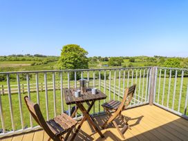 A balcony with two wooden chairs and a table with mugs and a thermos overlooking green fields and trees at Yr Adfa in Llangeitho near Tregaron