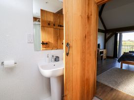 A bathroom sink and mirror with wooden door opening to a bedroom with desk chair bed and window at Yr Adfa in Llangeitho near Tregaron