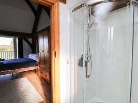 A bedroom with wooden furniture and a bed viewed through a doorway from a bathroom with a glass shower at Yr Adfa in Llangeitho near Tregaron
